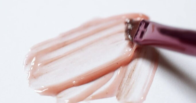 Smudging some peach pink lip-moisturizing balm, with a brush applicator on a white sheet of paper.