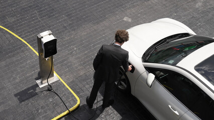 Progressive businessman unplugs charger plug from charging station to his electric car before...