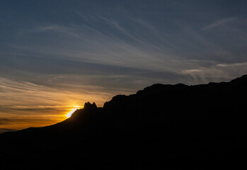 Silueta de las montañas al atardecer con el sol escondiéndose justo por el perfil de las montañas