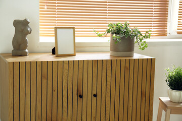 Blank frame with houseplant and decor on wooden commode in room