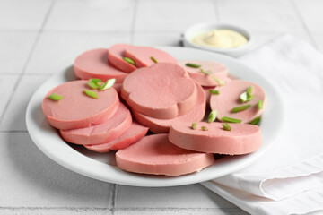 Plate with slices of tasty boiled sausage on white tile background