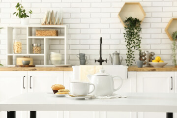 Interior of light kitchen with teapot, cup and snacks on table