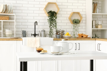 Interior of light kitchen with teapot, cup and snacks on table