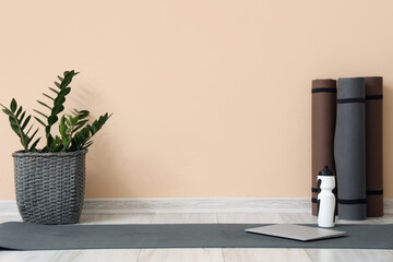 Fitness mats with bottle of water, laptop and plant near beige wall in room