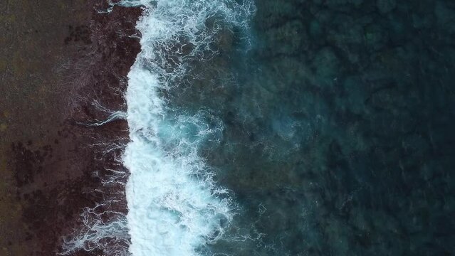 Aerial: top down shot of stormy waves crashing on reefs and coastline, slow motion. vertical format