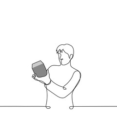 man stands holding a box in his hand and reads it or examines it in detail - one line art vector. concept receiving a gift, buying small equipment