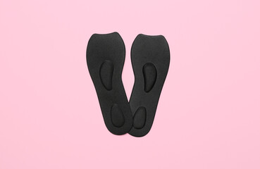 Pair of black orthopedic insoles on pink background