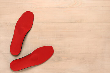 Pair of red orthopedic insoles on wooden background