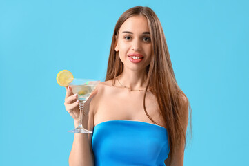 Beautiful young woman with glass of tasty martini on blue background