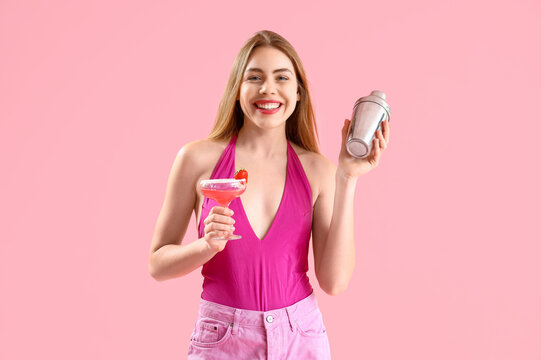 Beautiful young woman with glass of tasty strawberry cocktail and shaker on pink background