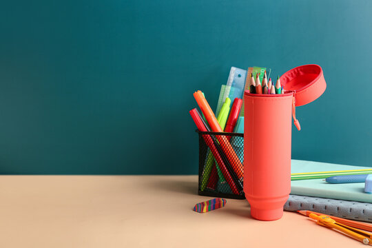 Red pencil case with school stationery on school desk near blackboard