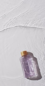 Vertical video of beauty product bottle in water with copy space on white background