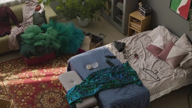 High angle no people shot of colorful messy bedroom with evening dresses scuttered on bed and couch and cosmetic products on makeup table after getting ready