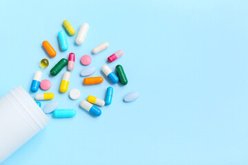 Overturned bottle with different pills on color background