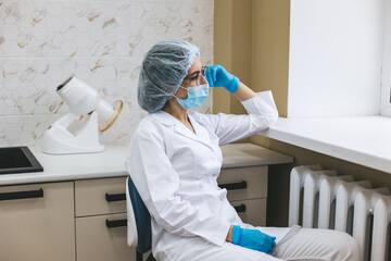 A young exhausted dentist sits by the window, reflecting on a long day of work. Doctor feels tired