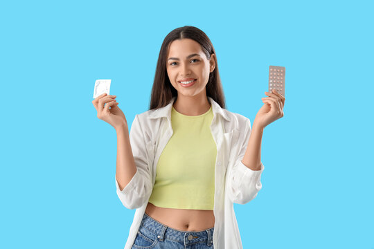 Young woman with condom and contraceptive pills on blue background