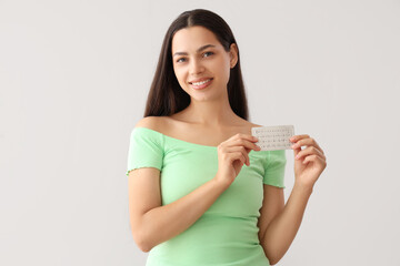 Young woman with contraceptive pills on light background