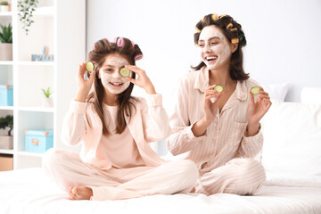 Little girl and her mother with hair curlers applying facial mask in bedroom