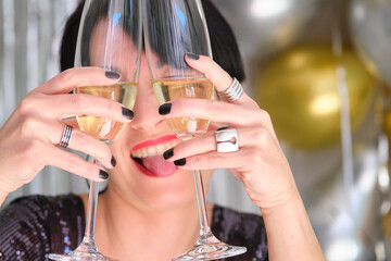 Caucasian woman with two glasses of champagne on her eyes celebrating New Year at a New Years Eve party.