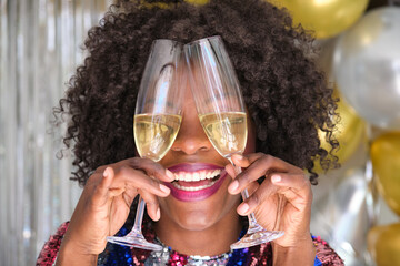 African woman with two glasses of champagne on her eyes celebrating New Year at a New Years Eve party.