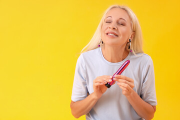 Mature woman with vibrator on yellow background