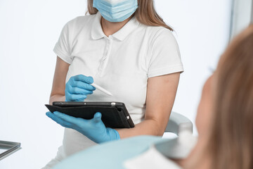 A dentist consults a patient at appointment at a medical clinic. Doctor enters data on electronic...