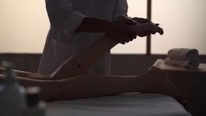 Badkamer foto achterwand Massagesalon Medium shot. Masseur, massage specialist giving a foot massage to his patient. Silhouettes of a woman and a man in the massaging room, spa procedure.