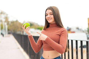 Teenager girl with an apple at outdoors and pointing it