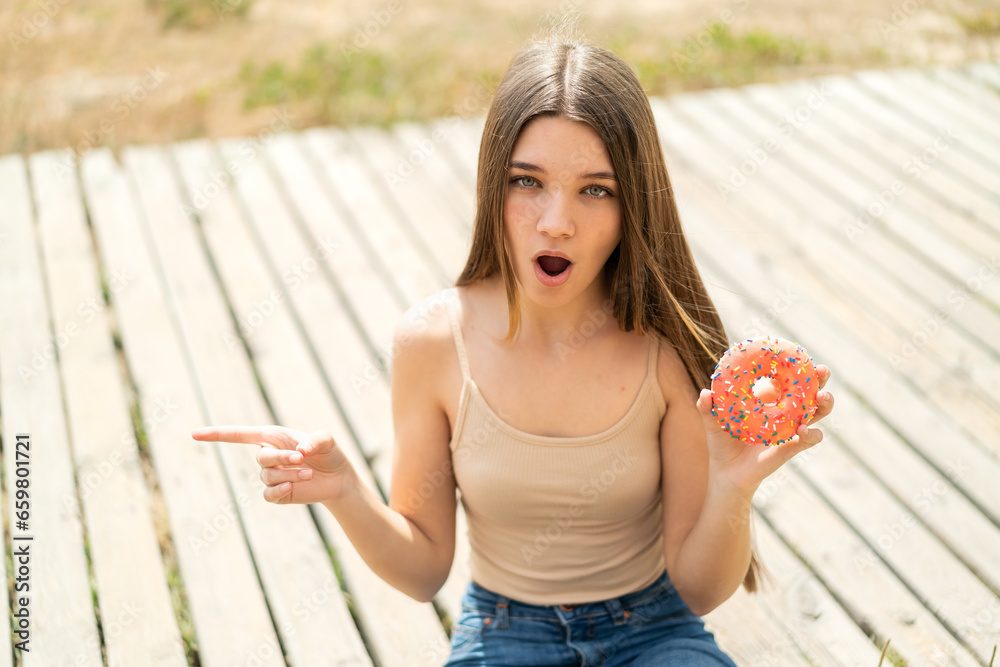 Canvas Prints Teenager girl holding a donut at outdoors surprised and pointing side