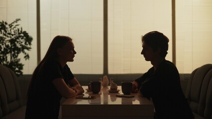 Silhouette of male and female sitting at the food bistro bar talking, drinking coffee and eating desserts.