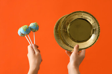 Female hands with tasty cake pops and plates for birthday party on color background, closeup