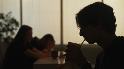 Silhouette of man at the fast food bistro bar drinking cola spending time, girl with man sitting at the back.