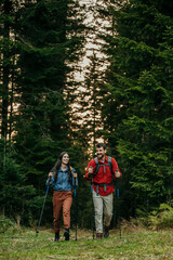 A couple with backpacks and walking sticks hiking in nature.