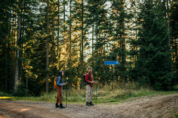 Pair of nature lovers with backpacks on a hiking adventure. Couple on forest crossroad.