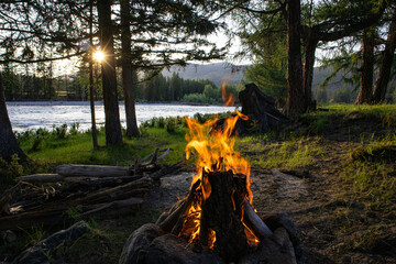 Bonfire near a mountain river. Camping by the river in the forest. The concept of adventure in the wild. Vacation concept.