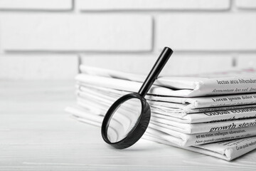 Morning newspapers and magnifying glass on table