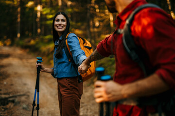 A multiethnic couple in love sets off on an invigorating hike, equipped with backpacks and walking poles to conquer the challenging yet rewarding trail - obrazy, fototapety, plakaty