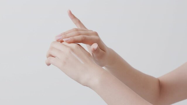 A woman's hand applying a white cosmetic formulation to the back of her hand. White background.