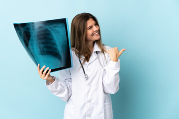 Young doctor woman holding radiography over isolated background pointing to the side to present a product