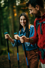 An adventurous and diverse couple eagerly explores a picturesque trail, their backpacks slung over their shoulders, and hiking sticks in hand