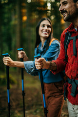 An adventurous and diverse couple eagerly explores a picturesque trail, their backpacks slung over their shoulders, and hiking sticks in hand