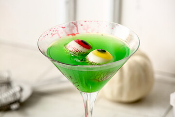 Glass of delicious green cocktail and eyes for Halloween celebration on light background, closeup