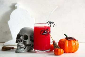 Glass of delicious red cocktail, skull and pumpkins for Halloween celebration on light background - obrazy, fototapety, plakaty