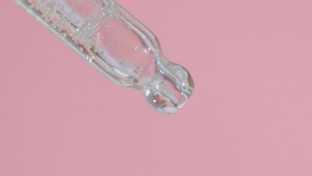 Glass pipette with transparent serum with reflections on a pink background, macro, beauty concept.