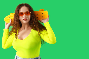 Beautiful young stylish woman with skateboard on green background - Powered by Adobe