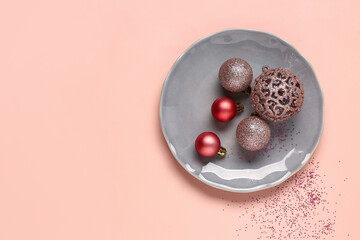 Plate with Christmas balls and confetti on pink background