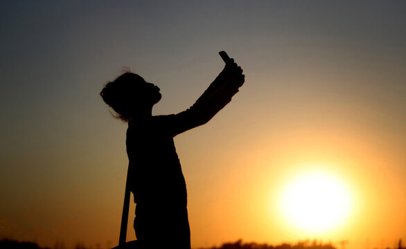 A girl stands at sunset and takes a picture with her mobile phone at sunset in a mountainous area north of the capital, Amman, where people like to stand there to take pictures and watch the sunset to