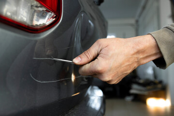 Close-up of a man's hand with a screwdriver scratching the body of a car, damaging someone else's property.