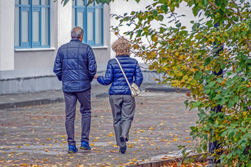 A man and a woman walk along the sidewalk on an autumn day