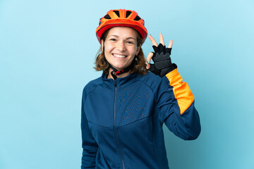 Young cyclist woman isolated on blue background showing ok sign with fingers